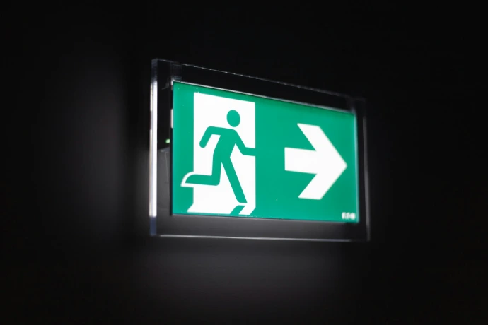 Illuminated green exit sign with a running figure and arrow.